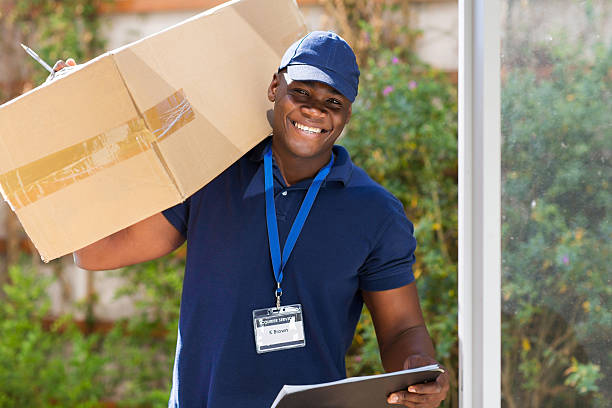 cheerful african courier standing with parcel at the door